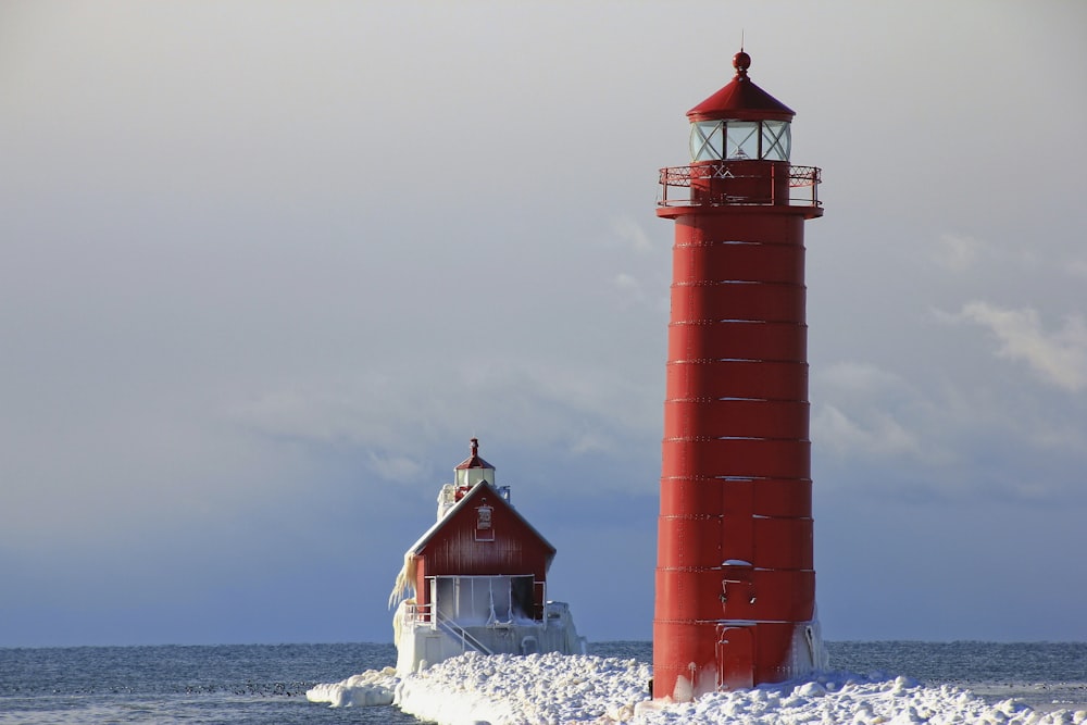 red lighthouse near white and red house beside body of water under white and blue sky