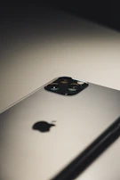 Smartphone placed on a white surface with soft shadows, focusing on the camera module.