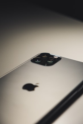 A close-up of a smartphone placed on a flat surface, highlighting its camera module and logo. The lighting creates a soft shadow, emphasizing the sleek design.