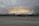 A large white aircraft with the inscription 'United States Dept. of Commerce' is parked on a tarmac. The sky in the background appears dramatic with layers of dark clouds and a faint glow of light, suggesting a sunrise or sunset.