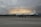 A large white aircraft with the inscription 'United States Dept. of Commerce' is parked on a tarmac. The sky in the background appears dramatic with layers of dark clouds and a faint glow of light, suggesting a sunrise or sunset.