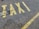 Yellow letters painted on a rough asphalt surface spell out the word 'TAXI'. The paint appears slightly worn and is accompanied by a yellow line running parallel to the word.