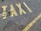 Yellow letters painted on a rough asphalt surface spell out the word 'TAXI'. The paint appears slightly worn and is accompanied by a yellow line running parallel to the word.