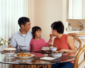 a man, woman and child sitting at a table eating food