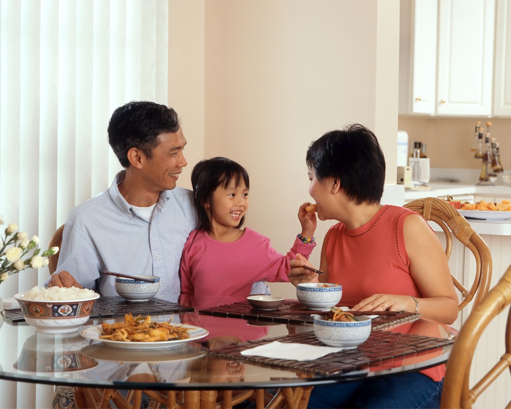 a man, woman and child sitting at a table eating food
