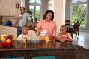 A family enjoying Tropical Twist juices together in a sunny kitchen.