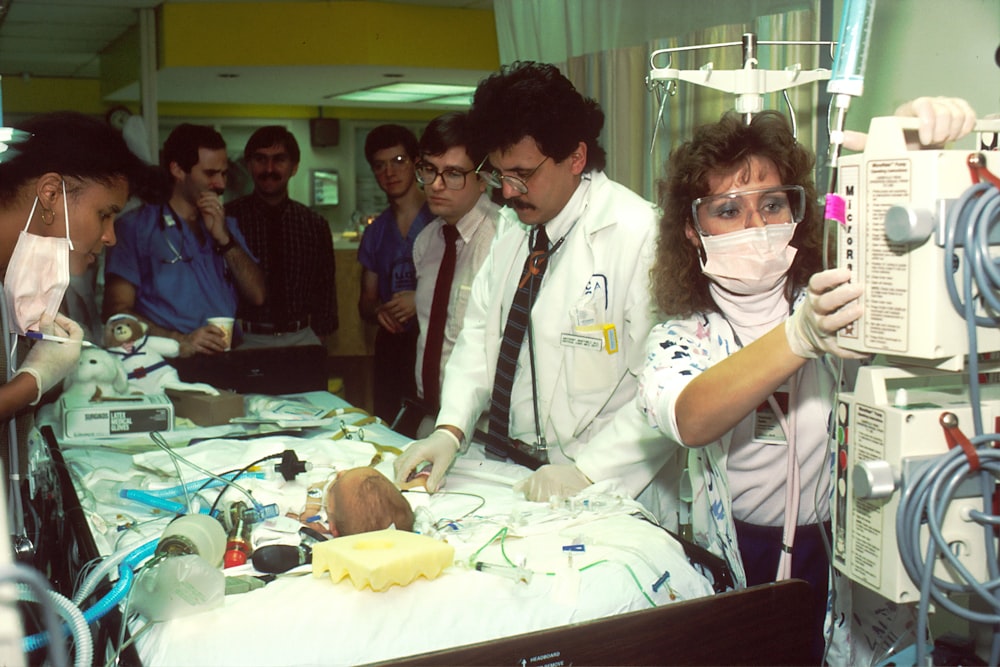 people beside baby lying on bed with medical apparatuses