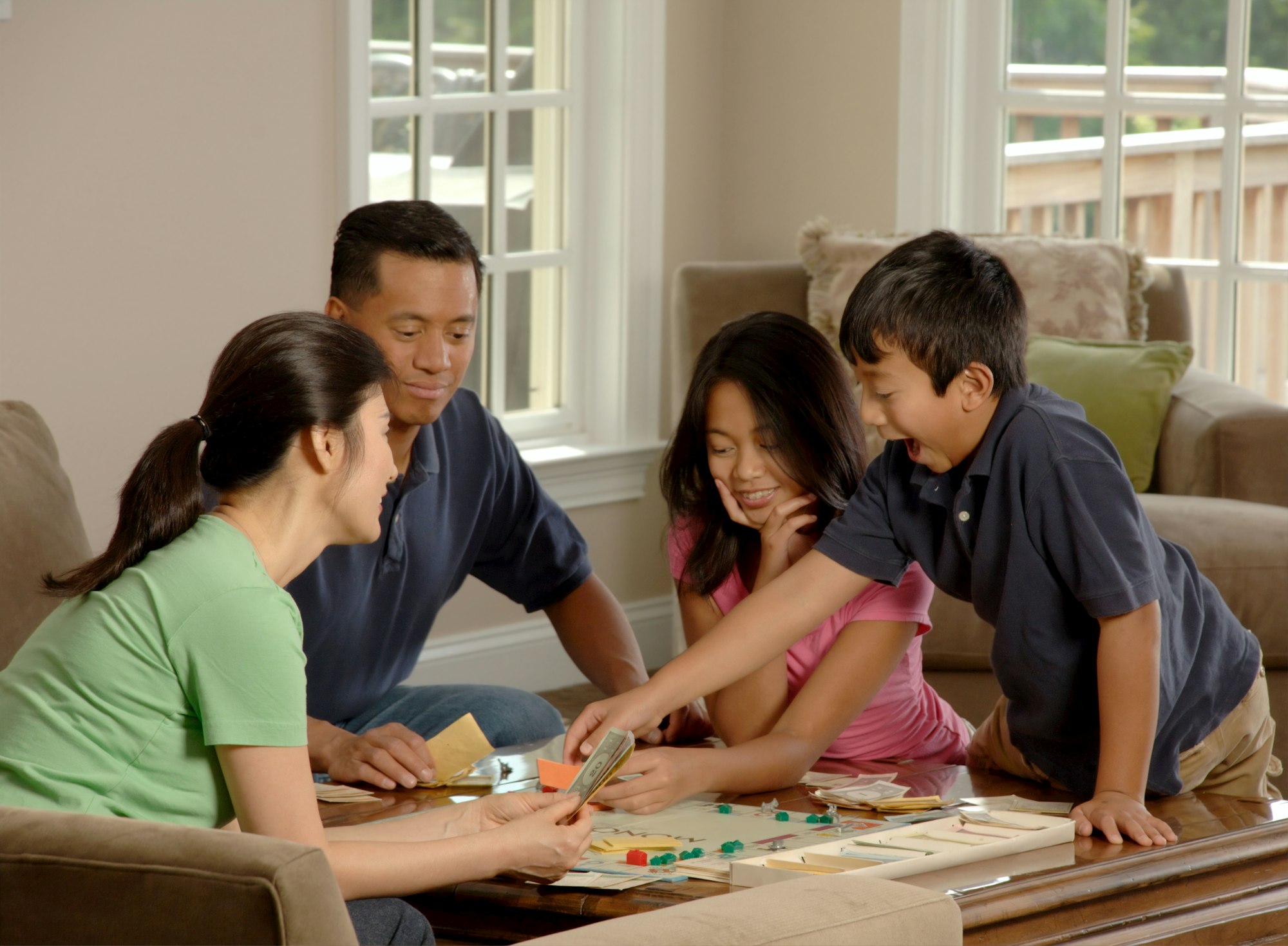 Family Playing A Board Game. An Asian family \(adult male and female and two adolescents, male and female\) sitting around a coffee table playing a board game. Photographer Bill Branson