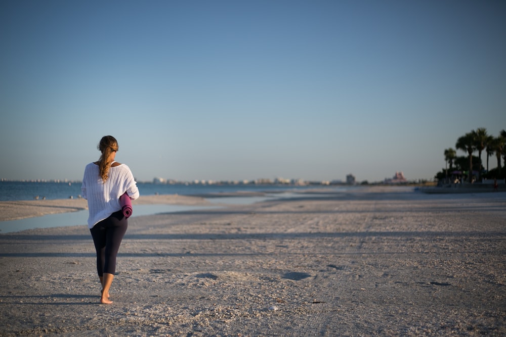 woman wearing white shirt and black capris walking on seashore during daytime