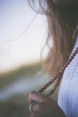 Close-up of hands weaving macramé knots with natural stone beads in warm light.