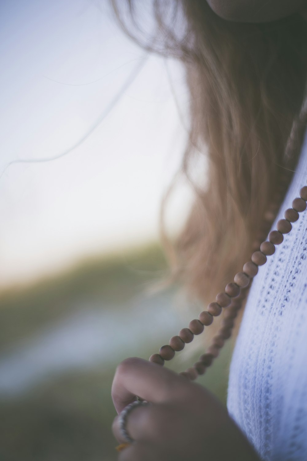 person wearing white top and beaded brown necklace