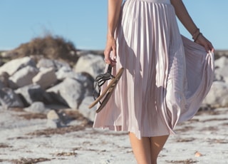 woman wearing white skirt holding black leather flat sandals standing