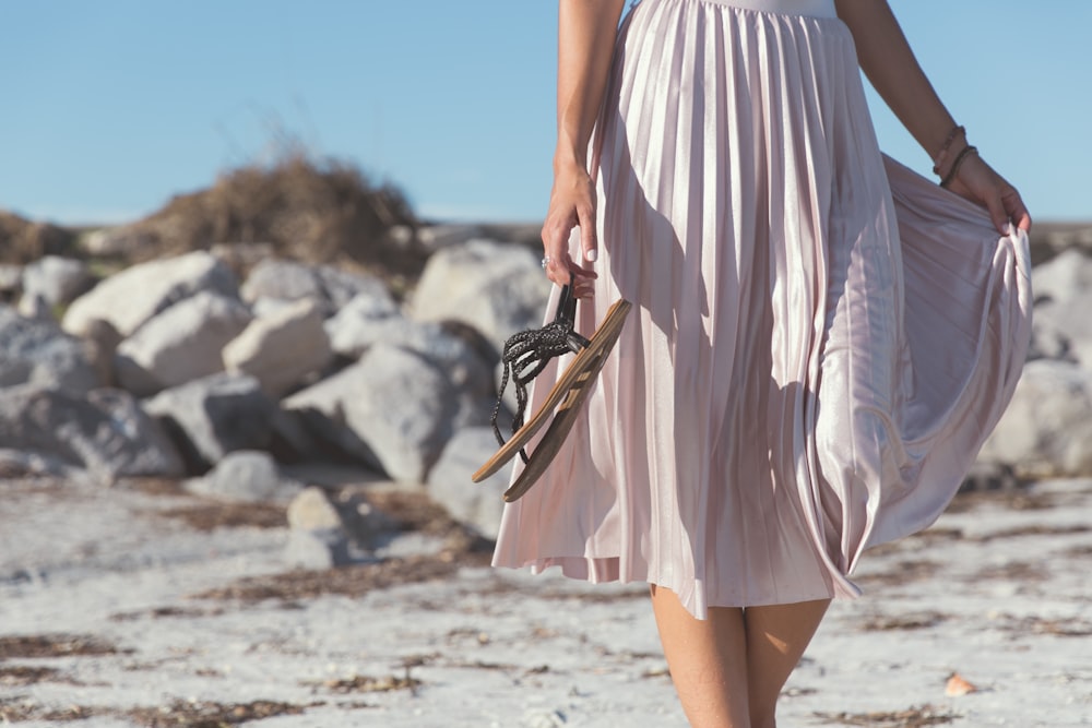 Femme portant une jupe blanche tenant des sandales plates en cuir noir debout