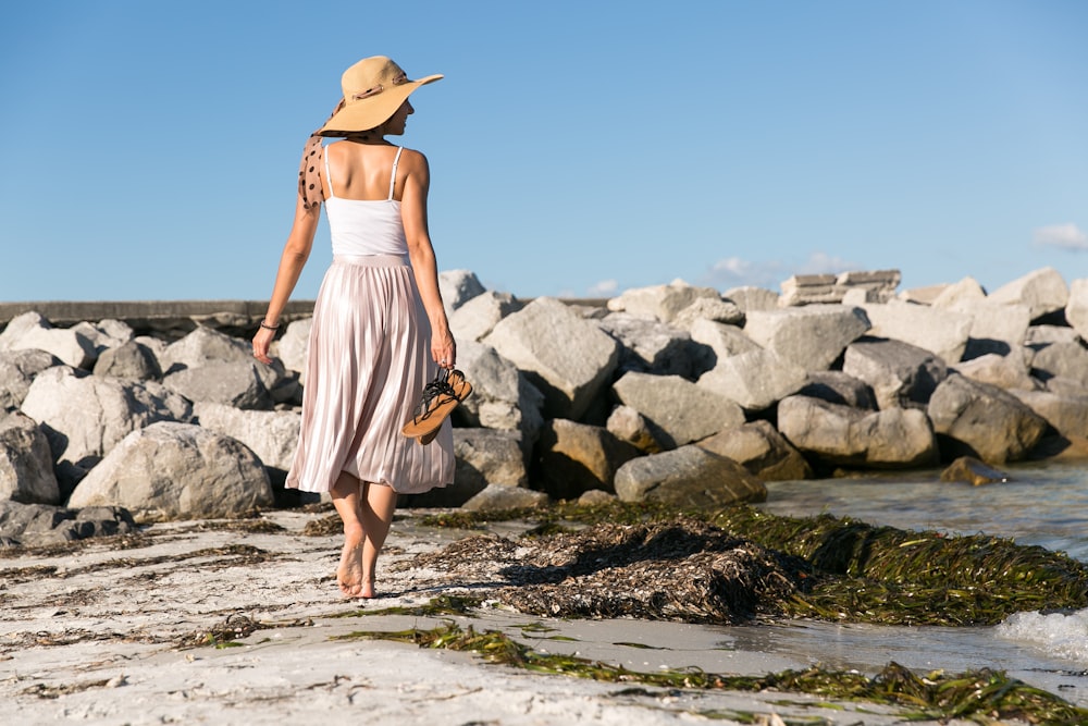 femme portant un chapeau de soleil marron marchant sur le bord de la mer