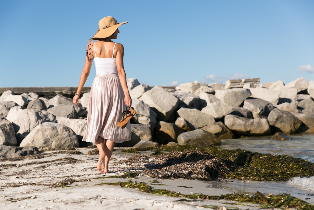 Frau mit braunem Sonnenhut geht am Meeresufer spazieren