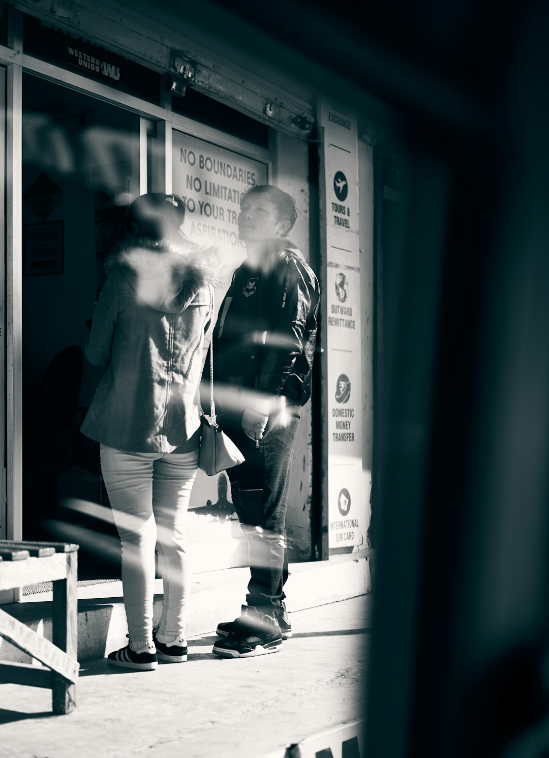 grayscale photography of two people standing near glass window