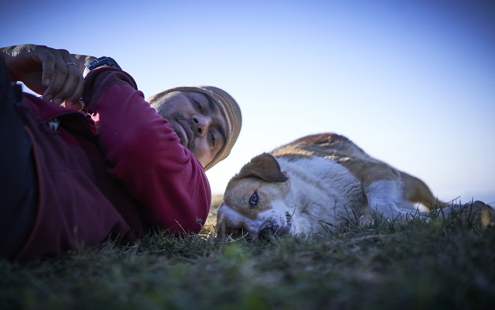 fotografia macro di uomo che indossa giacca sdraiato sull'erba vicino al cane bianco e marrone a pelo corto