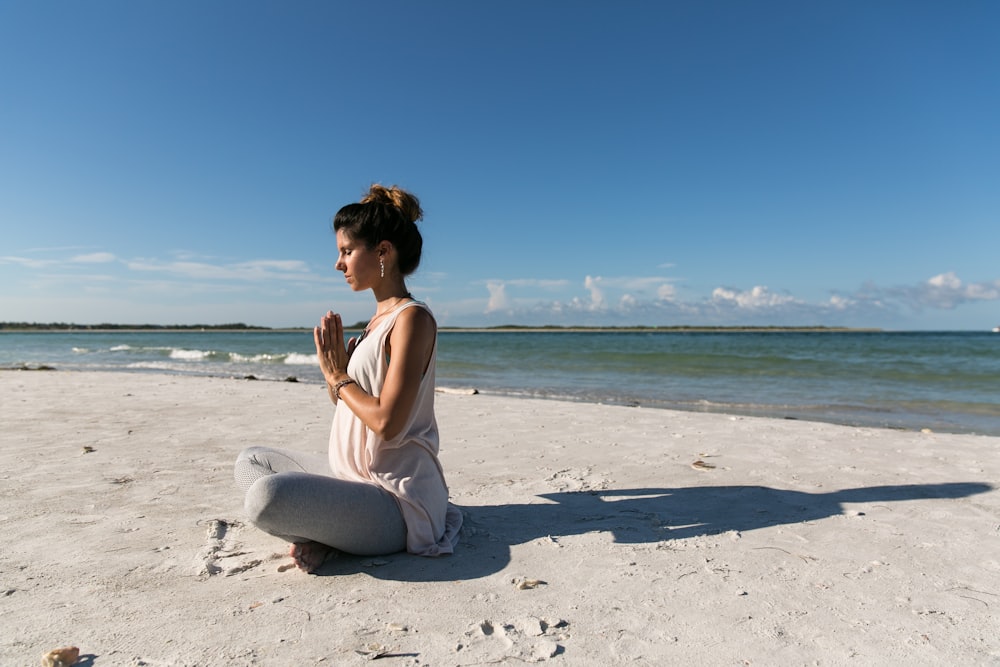 mulher orando e sentada na praia de areia durante o dia