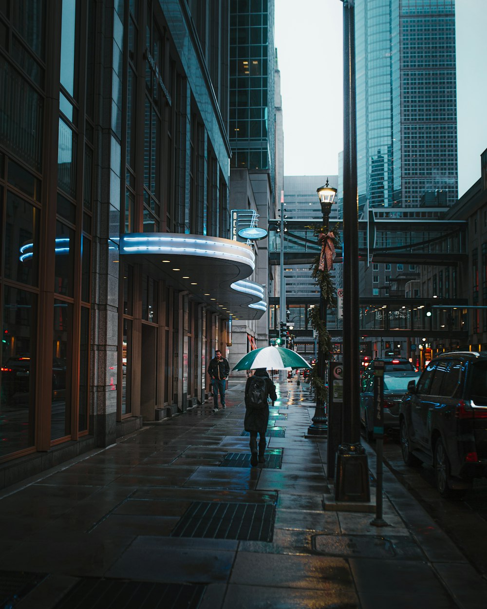 person using umbrella while walking on pathway and different vehicles on road during night time