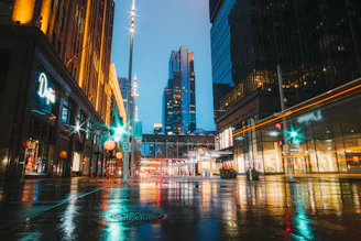A vibrant cityscape at dusk with glowing lights reflecting on wet streets.