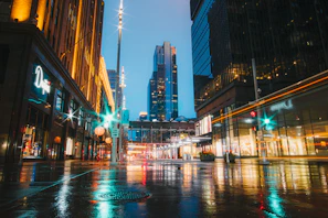 A vibrant cityscape at dusk with glowing lights reflecting on wet streets.