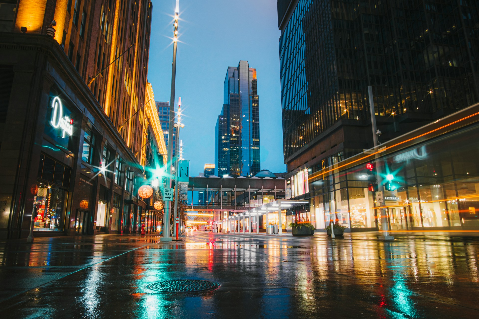 A vibrant cityscape at dusk with glowing lights reflecting on wet streets.