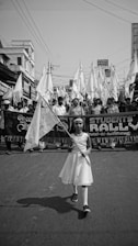 grayscale photography of girl holding banner while walking on street near crowd of people