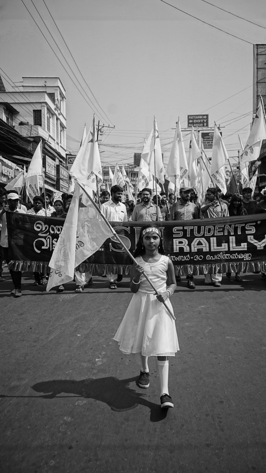 grayscale photography of girl holding banner while walking on street near crowd of people