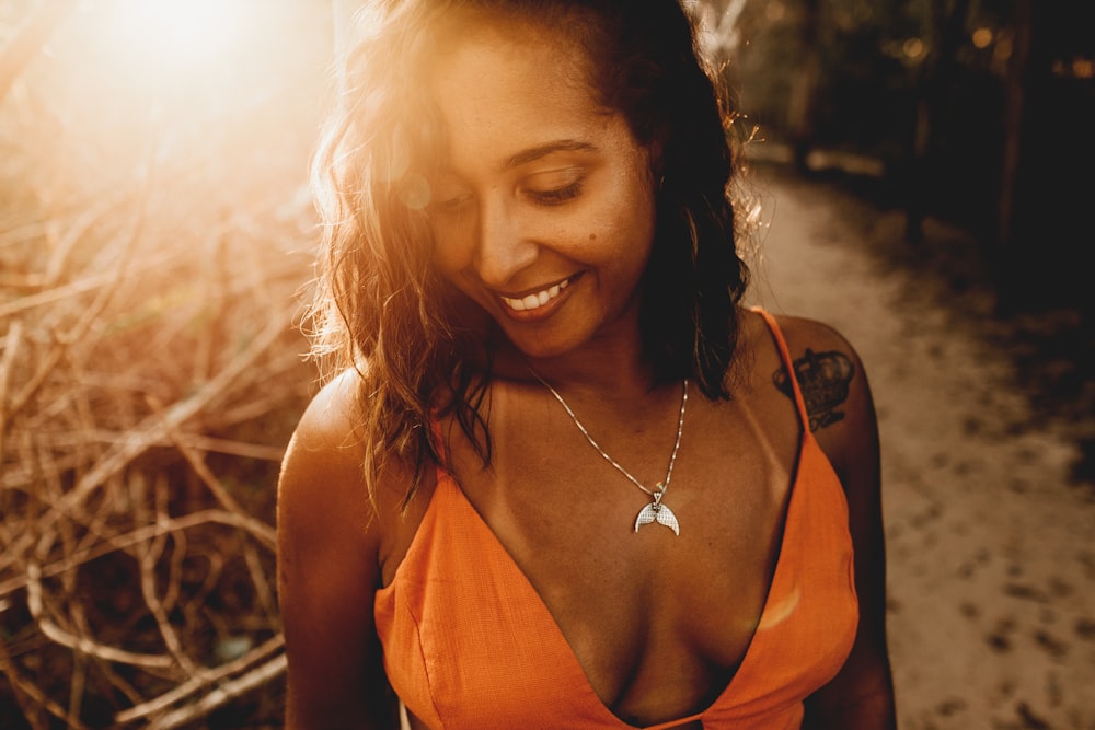 smiling woman wearing orange spaghetti strap top standing while looking down