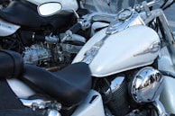 Several motorcycles are parked closely together. The focus is on a white motorcycle with chrome accents including the mirrors, engine parts, and instrument panel on the fuel tank. The seats are black and leather, and the motorcycles appear to be in good condition.