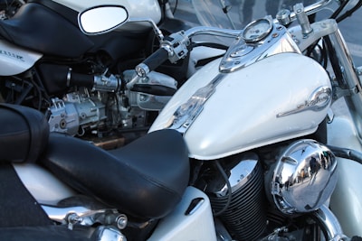 Several motorcycles are parked closely together. The focus is on a white motorcycle with chrome accents including the mirrors, engine parts, and instrument panel on the fuel tank. The seats are black and leather, and the motorcycles appear to be in good condition.