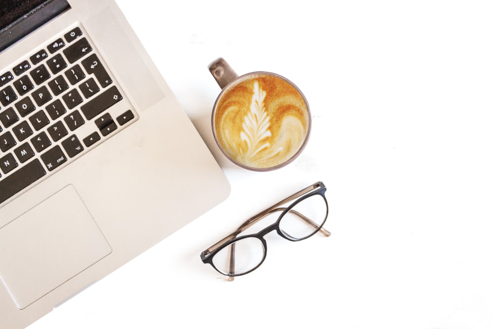 black and white laptop computer near cappuccino and black framed eyeglasses