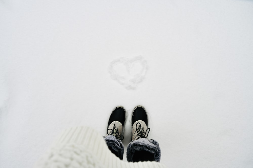 person wearing black-and-white shoes standing on snowy field with heart drawing