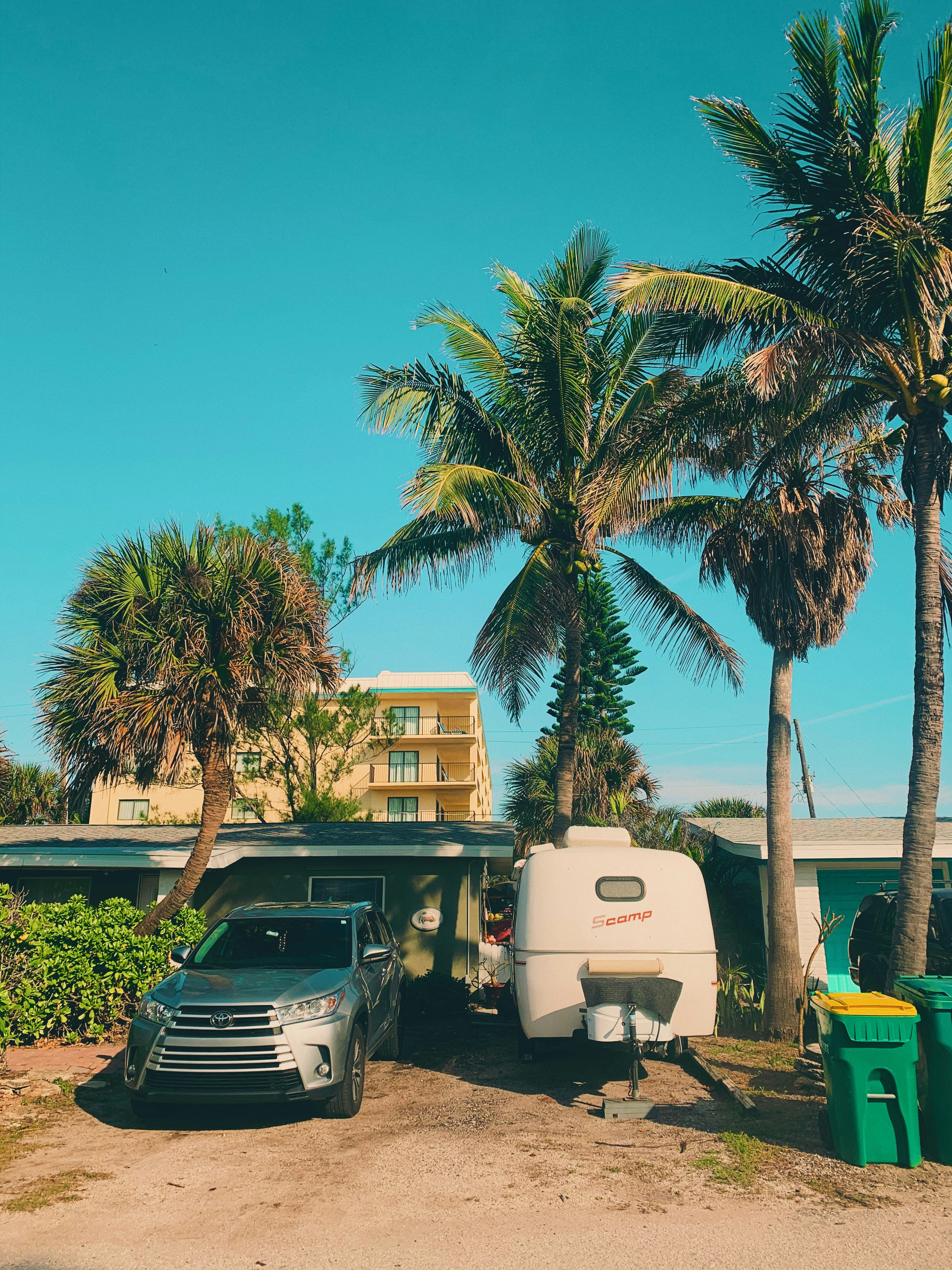 gray vehicle parked beside camper trailer near trees and public trash bins