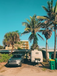 gray vehicle parked beside camper trailer near trees and public trash bins