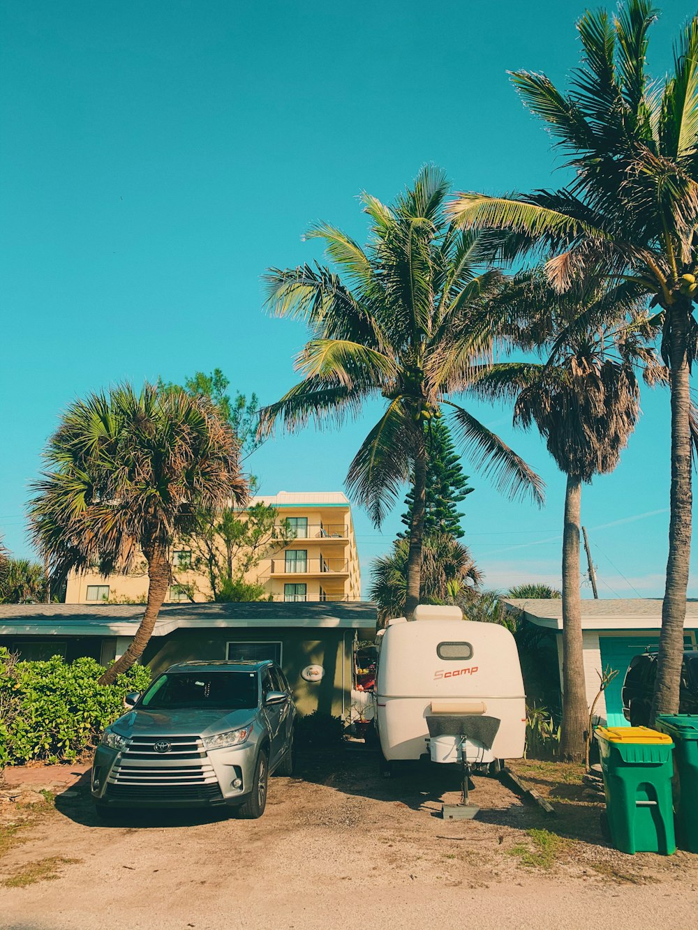 gray vehicle parked beside camper trailer near trees and public trash bins