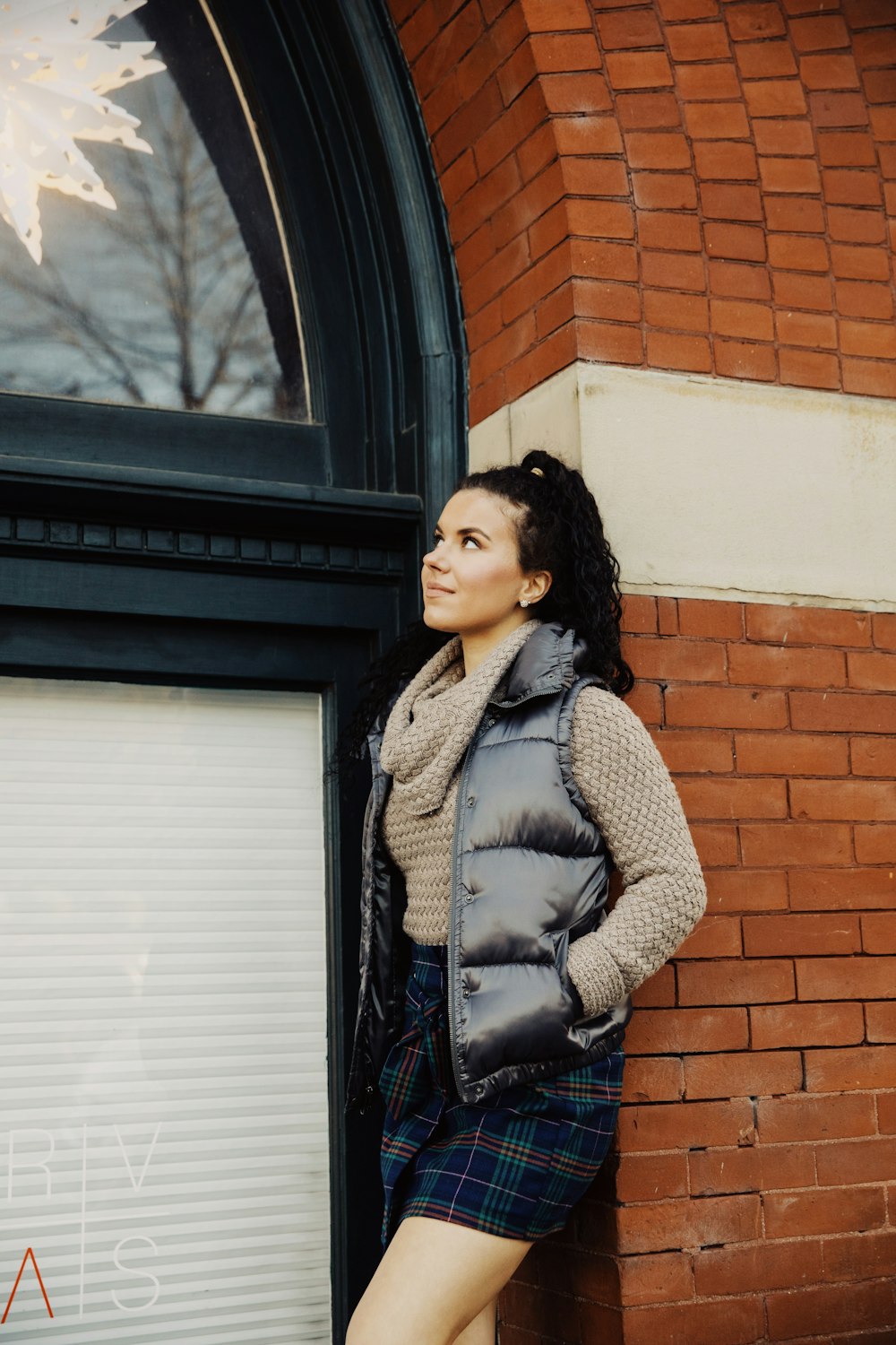 woman wearing brown cowl-neck sweater standing and leaning against the wall while looking up