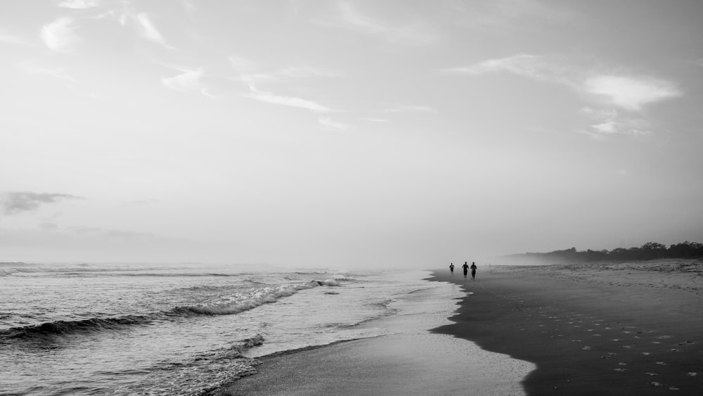 a couple of people standing on top of a beach next to the ocean