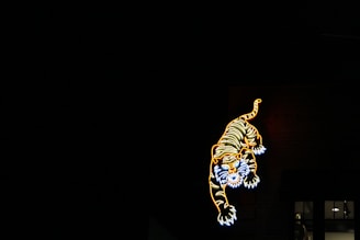 A brightly colored neon sign of a tiger is illuminated against a dark backdrop. The tiger appears in a leaping or jumping pose, with vivid shades of orange, yellow, and white outlining its shape.