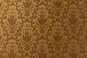 A vintage-style wallpaper with an intricate, repeating floral and damask pattern in shades of brown and beige. The design features ornate, symmetrical motifs that create a sense of elegance and classic decor.
