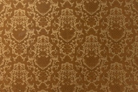 A vintage-style wallpaper with an intricate, repeating floral and damask pattern in shades of brown and beige. The design features ornate, symmetrical motifs that create a sense of elegance and classic decor.