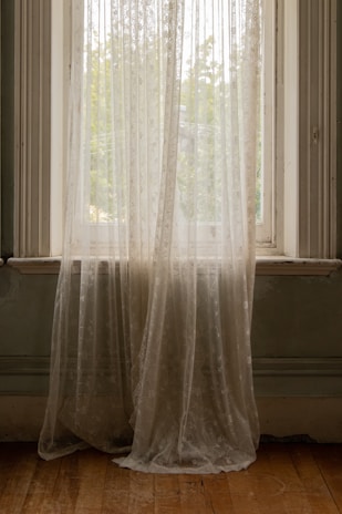 A cozy living room with soft sheer curtains and elegant curtain rods framing a sunlit window.
