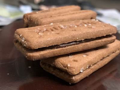 A close-up view of several rectangular cookies stacked on top of each other. The cookies have a sandwiched chocolate filling and are sprinkled with coarse sugar crystals. The background appears blurred, emphasizing the focus on the cookies.