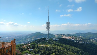 A panoramic view of a tall mobile tower standing on open land surrounded by greenery.