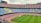 A large empty football stadium with multi-colored seating. The seats are arranged in patterns that spell out phrases. The grass pitch is well-maintained and there are advertisements around the stadium.