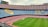 A large empty football stadium with multi-colored seating. The seats are arranged in patterns that spell out phrases. The grass pitch is well-maintained and there are advertisements around the stadium.