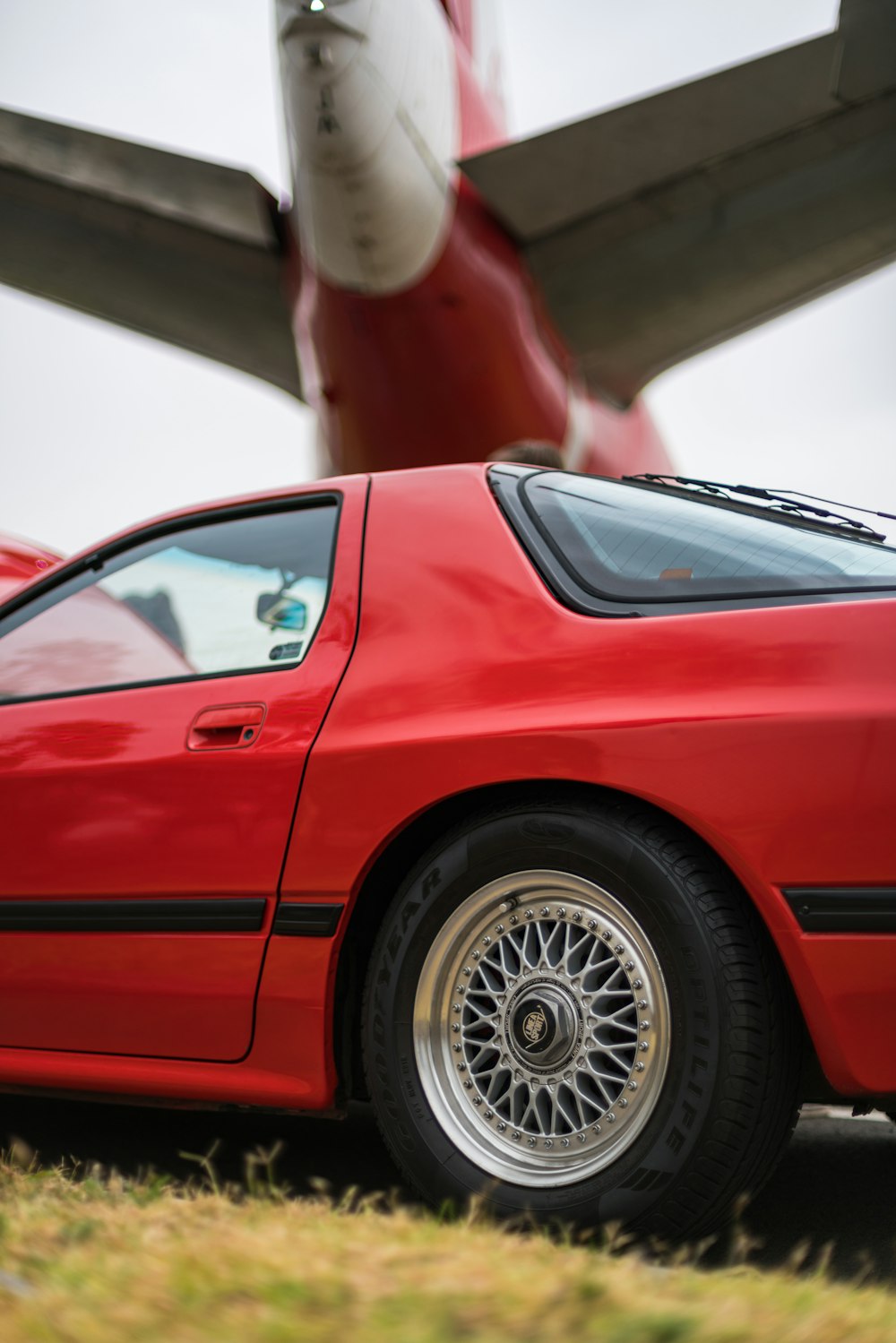 red coupe under an airplane