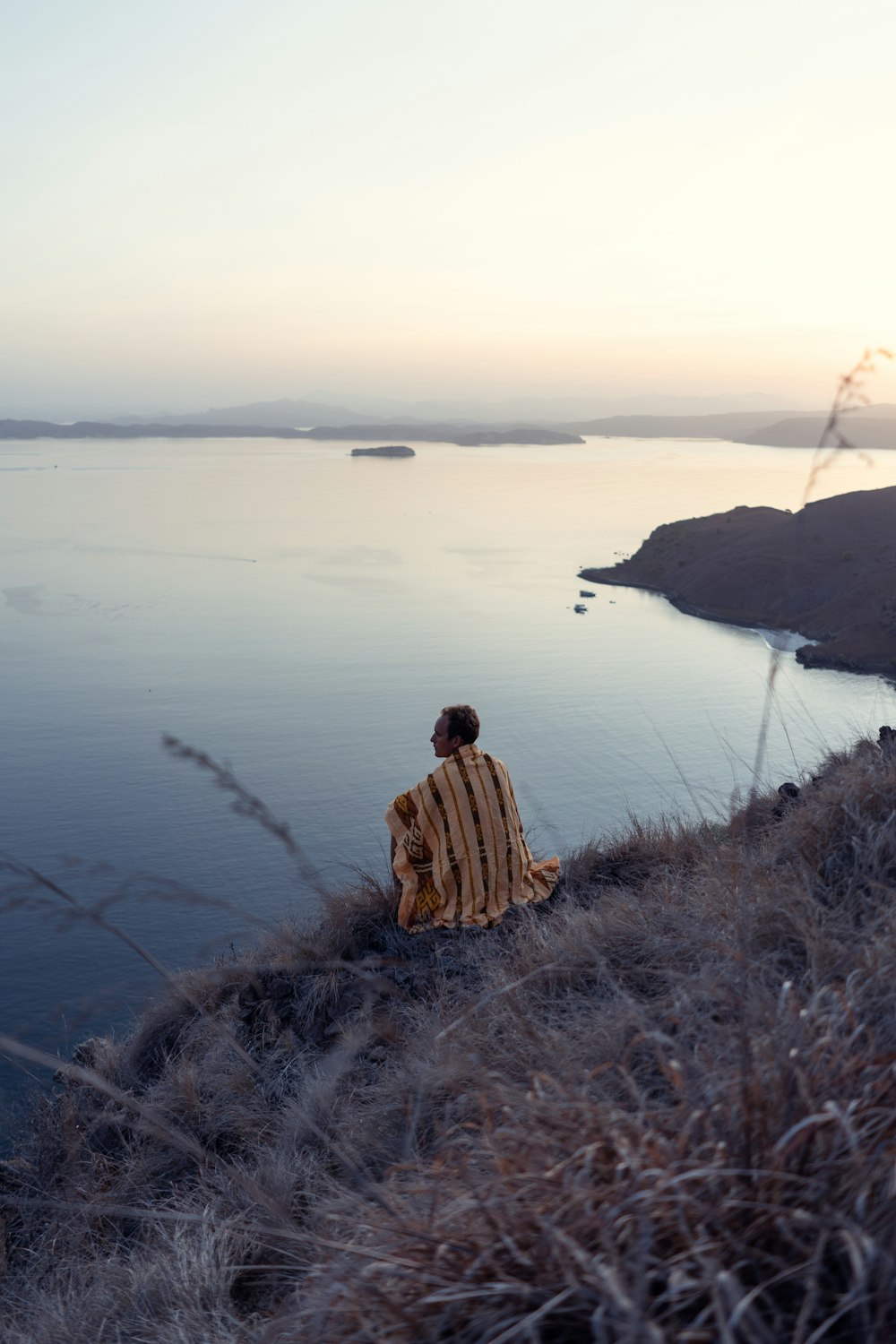 man sitting on cliff near body of water