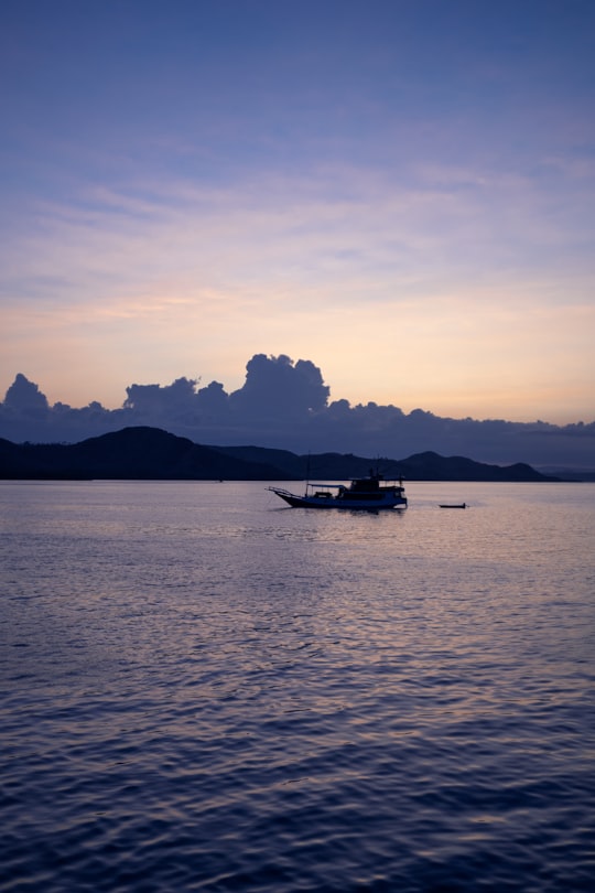 silhouette photography of a boat floating in the sea under a calm blue sky in Komodo National Park Indonesia