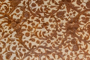 Intricate patterns of floral and foliage designs are carved elegantly into a surface, with detailed depictions of leaves, flowers, and fruits intertwined across the textured background. The craftsmanship reflects a harmonious blend of natural elements creating a vintage or classical aesthetic.